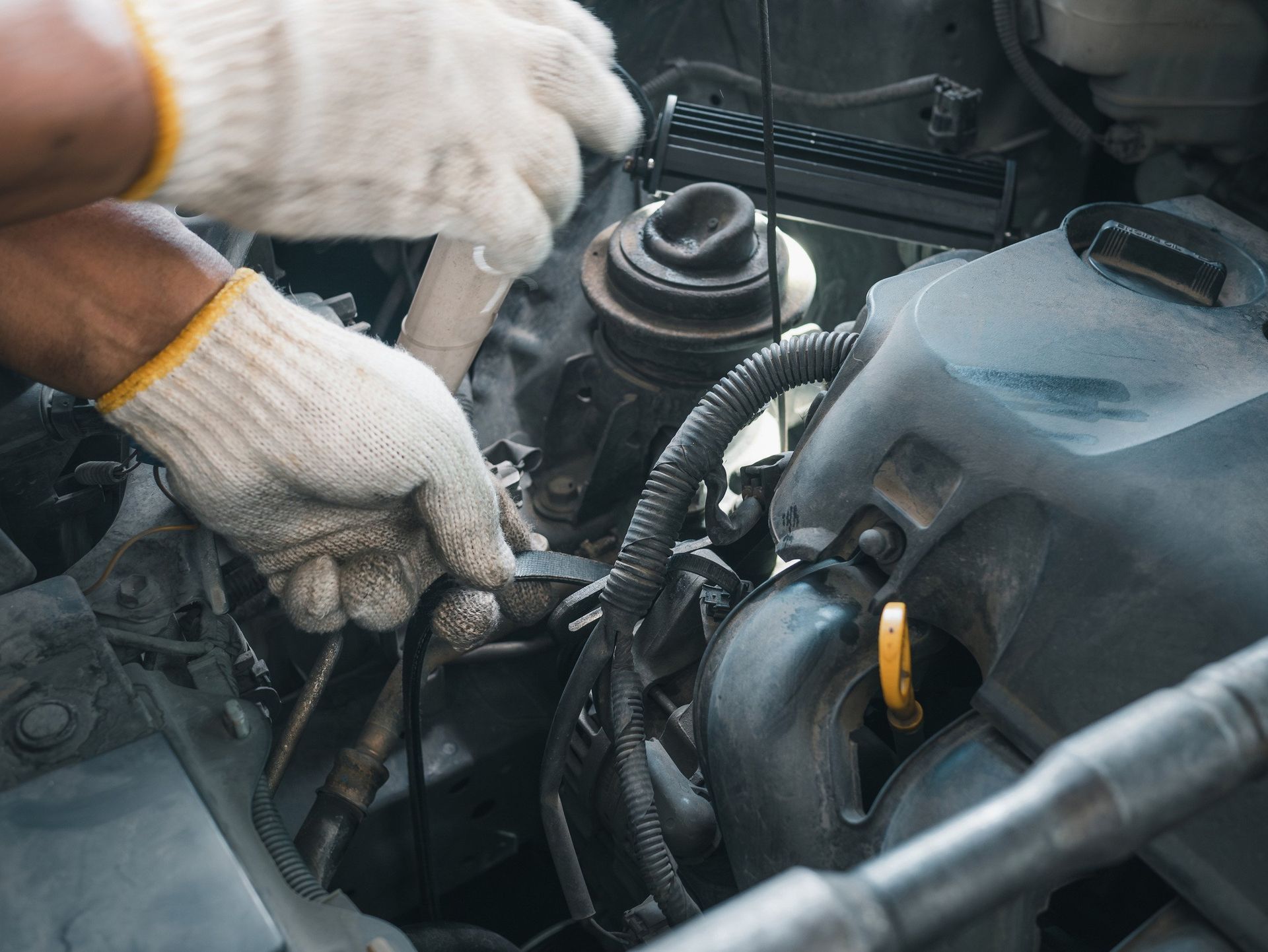 A man wearing gloves is working on the engine of a car.