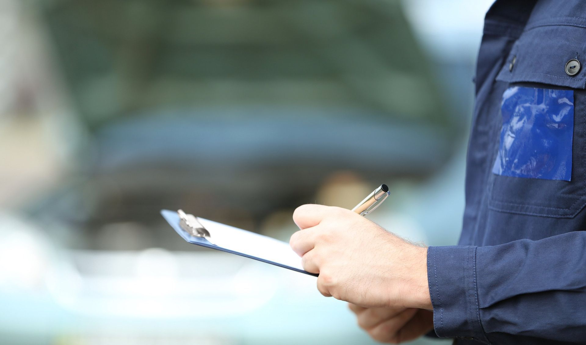 A man is holding a clipboard and a pen in front of a car.