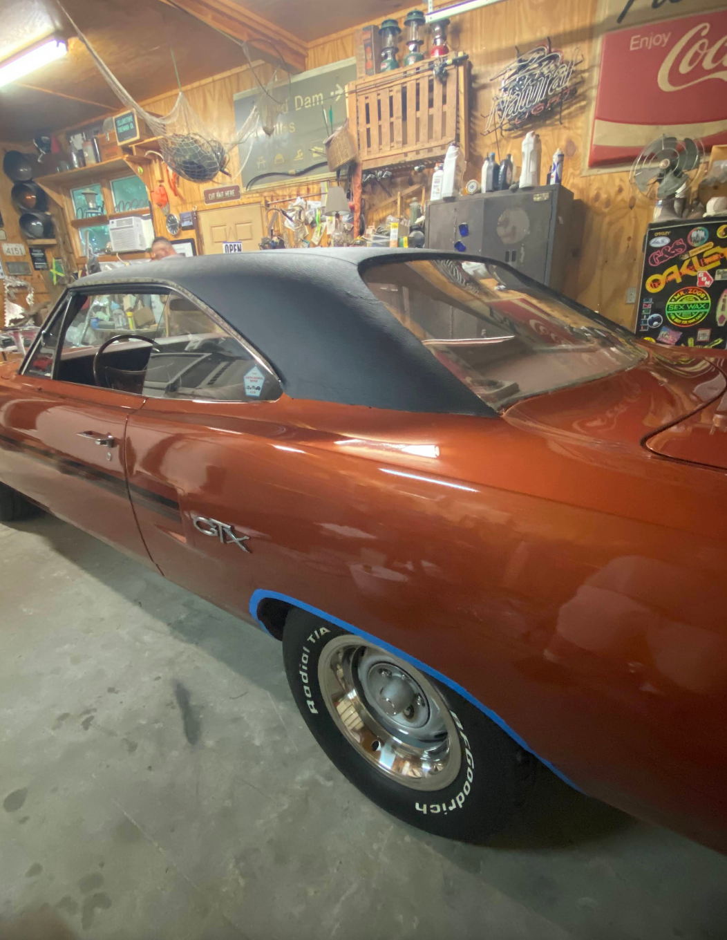 A red car is parked in a garage next to a coca cola sign.