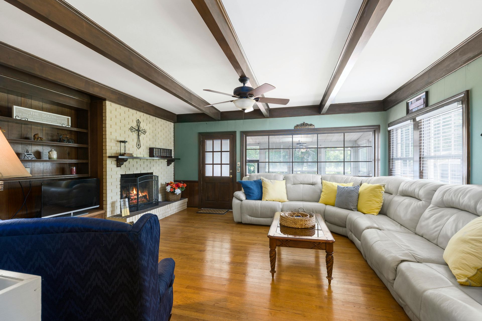 Living room with a sectional sofa, fireplace, wood beams, and wooden floors.
