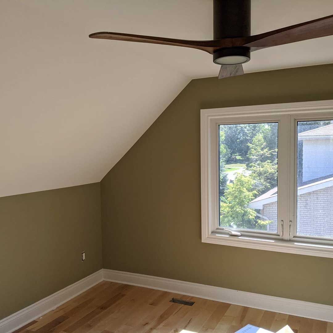 Room with sloped ceiling, olive green walls, wood floor, window with a view, and a ceiling fan.