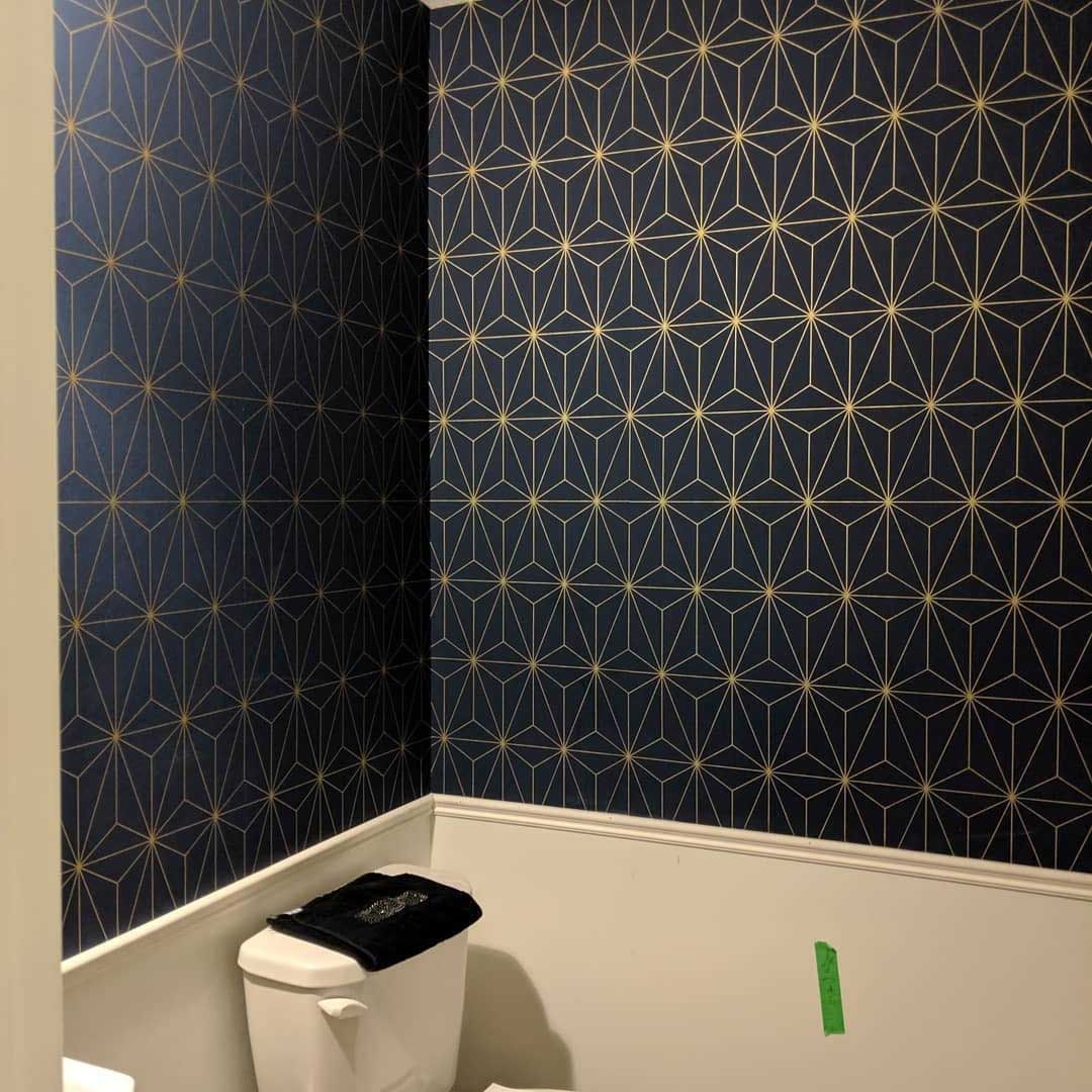 Dark blue and gold geometric wallpaper in a bathroom with white wainscoting and a toilet.