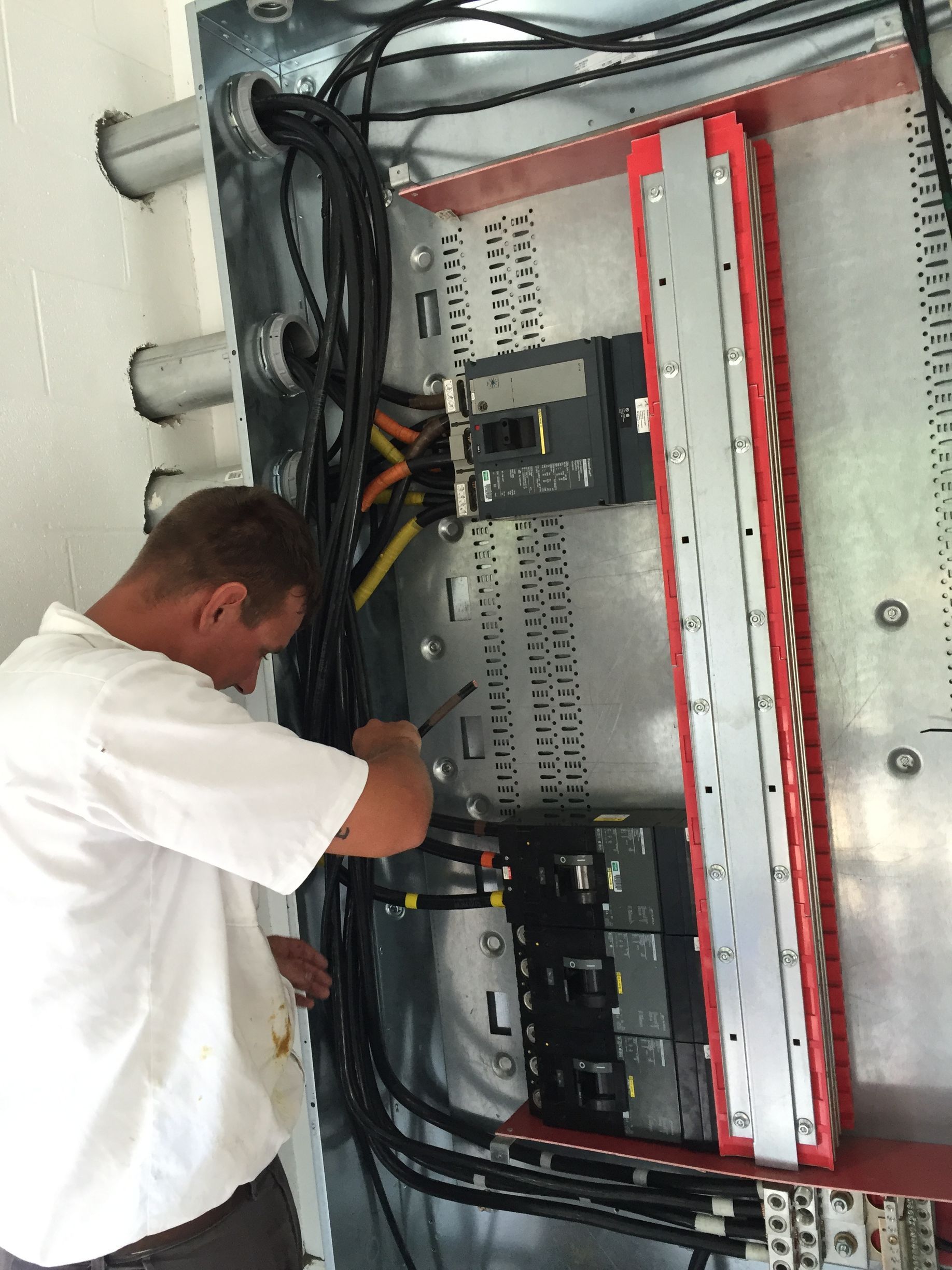 Electrician working inside an electrical panel, connecting wires. Panel is mounted in a wall, red trim on the inside.