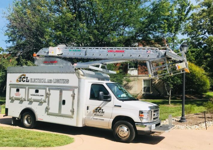 White electrical service truck with extended boom parked on grass next to a house.