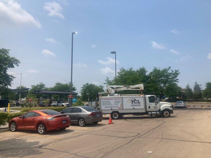 Orange car and gray car parked in front of a white work truck with a raised crane, under a blue sky.