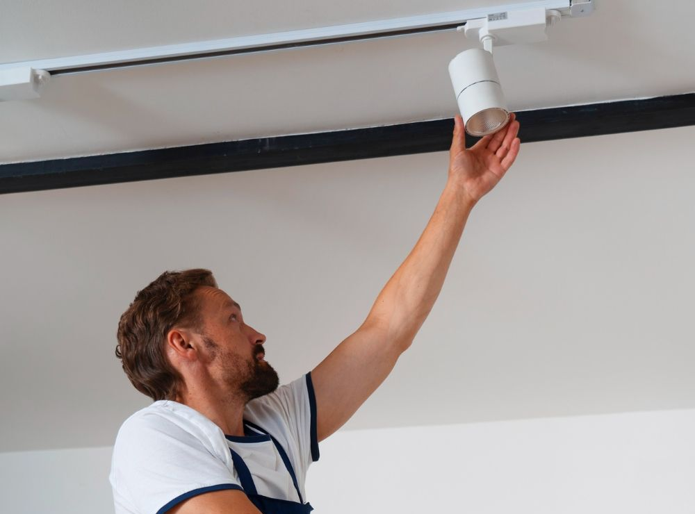Man installing a track lighting fixture on a white ceiling.