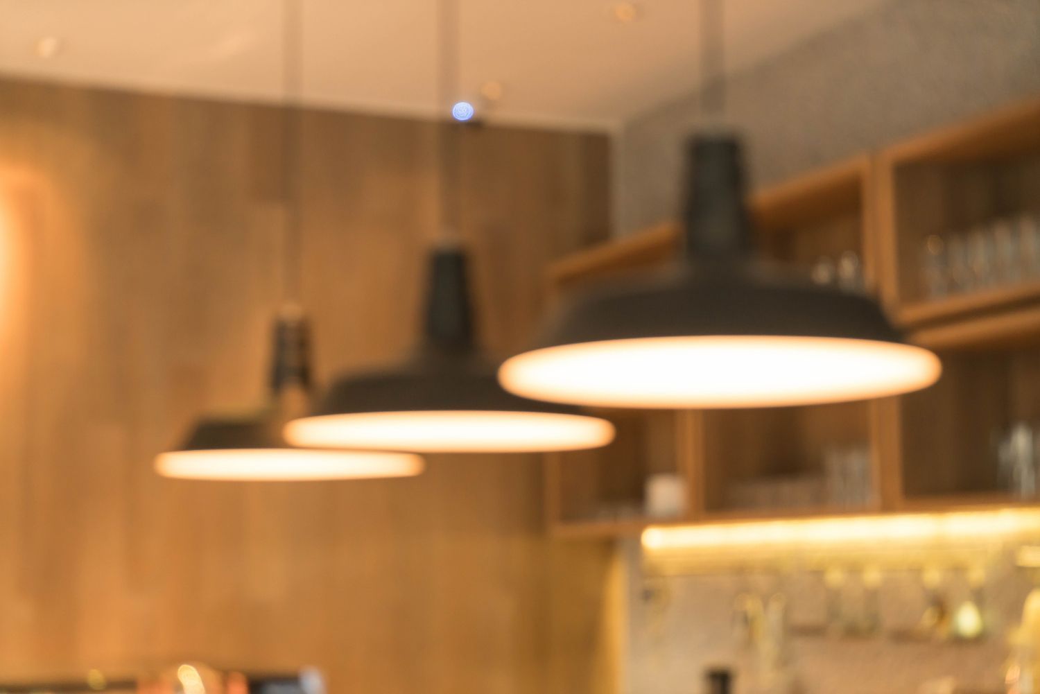 Three black pendant lights with white light illuminating a wooden counter and shelves.