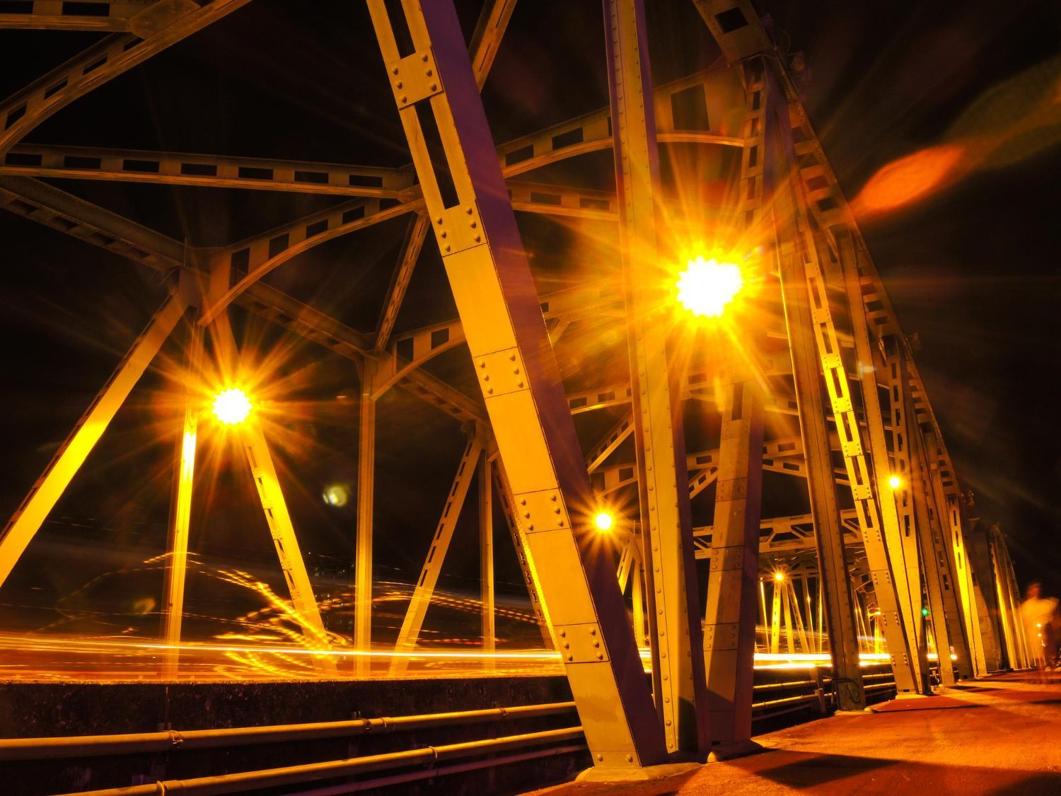 Illuminated bridge at night with bright orange lights and streaks of light from passing vehicles.
