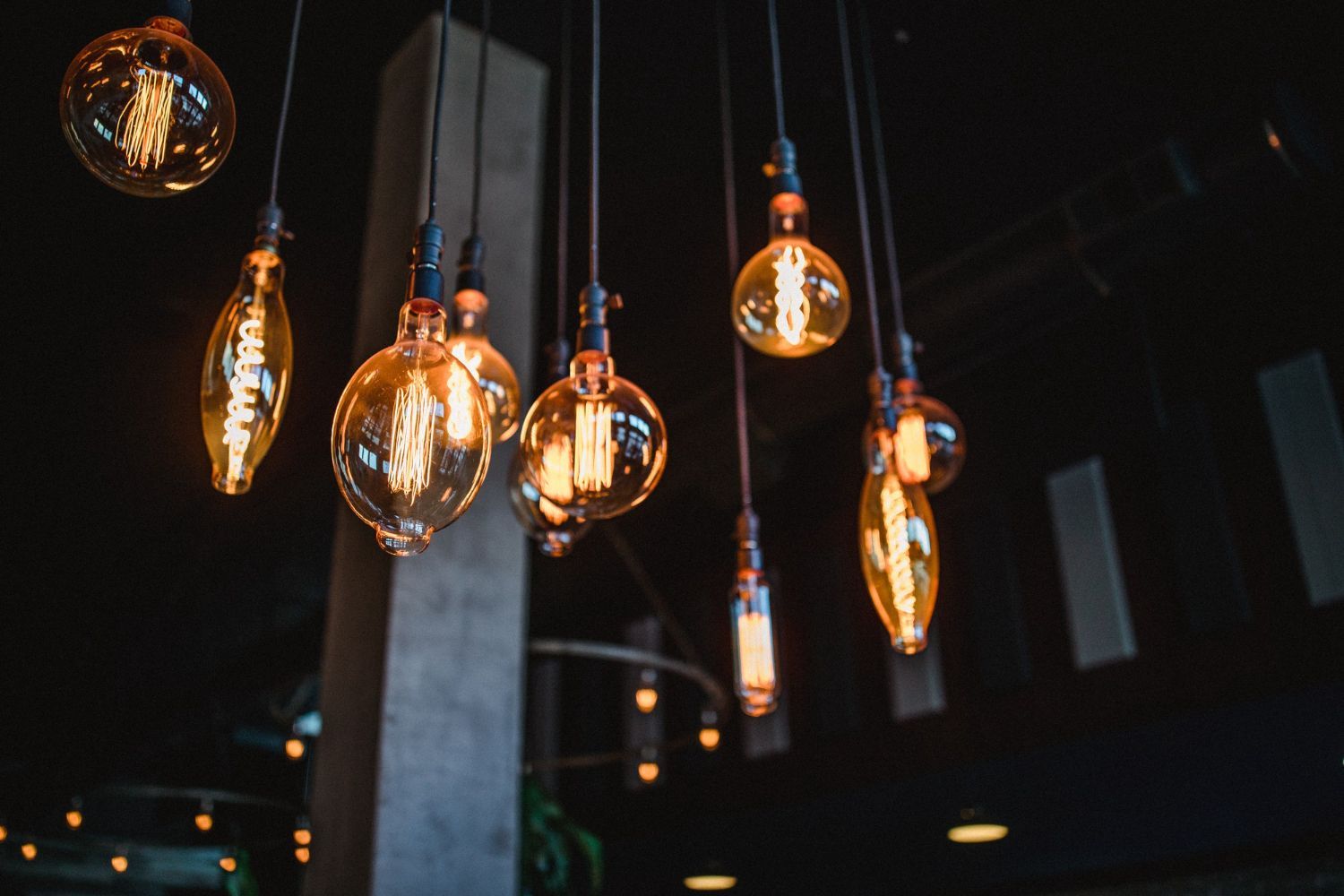 Edison-style light bulbs hang from a dark ceiling, glowing with warm orange light.