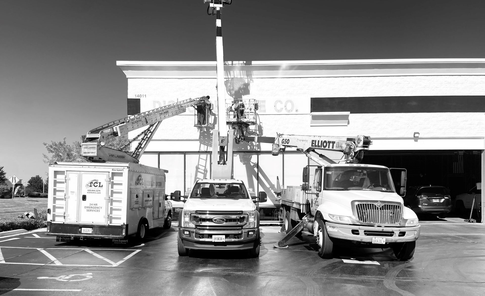 Three utility trucks parked in front of a building; lift equipment extended, workers present.