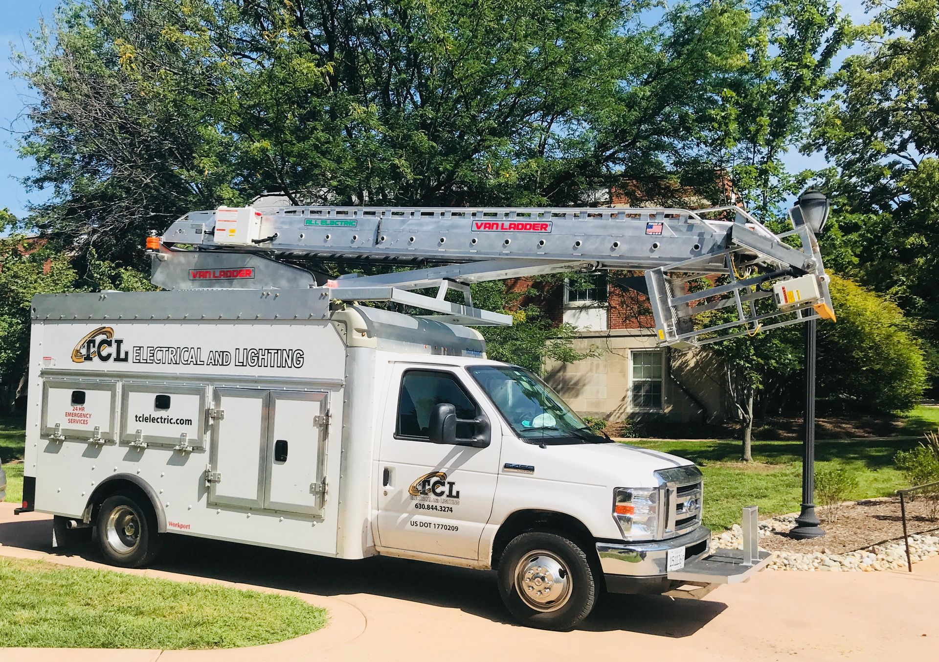 White utility truck with an aerial lift parked on a lawn in front of a house.