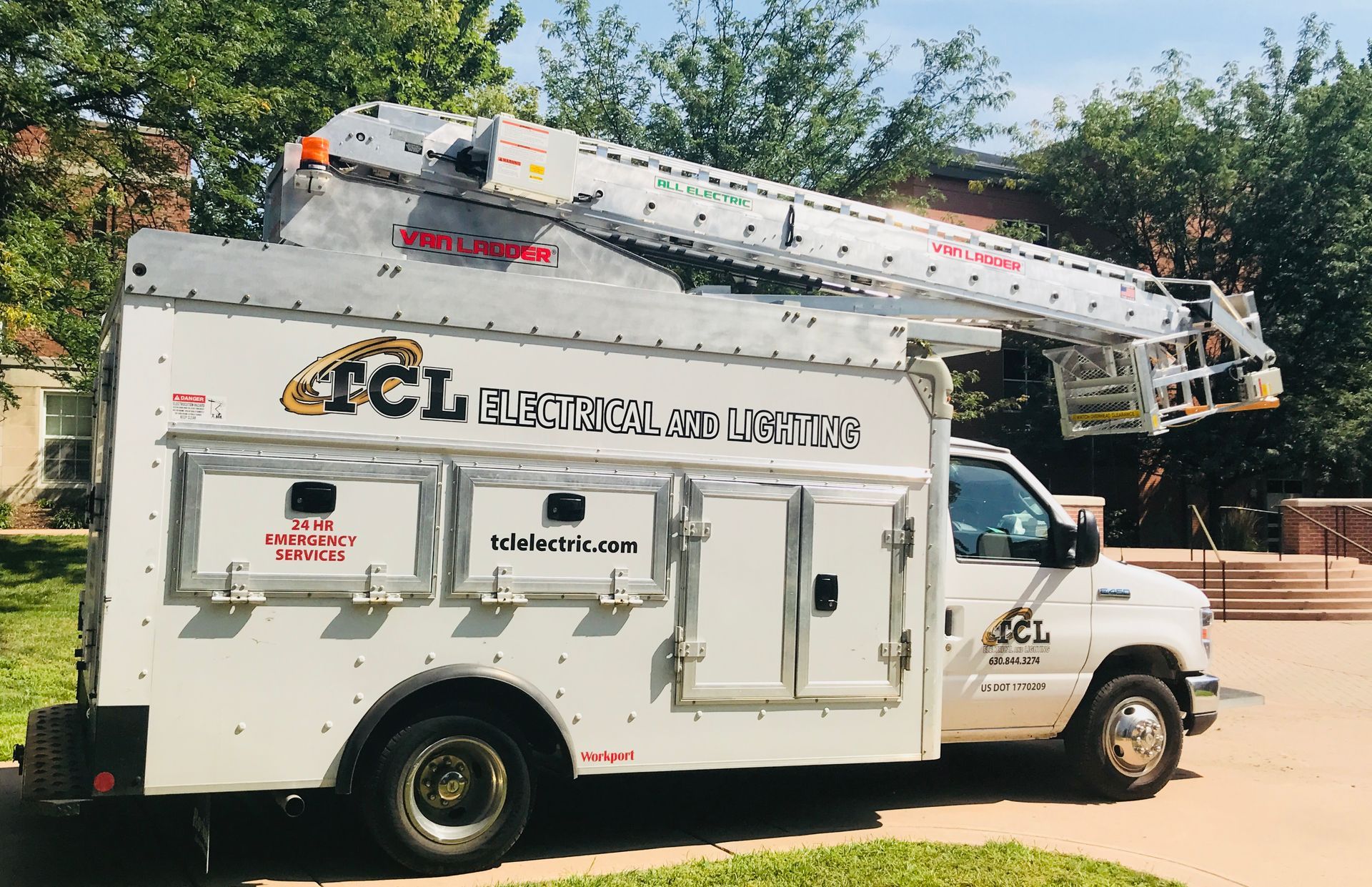 White TCL Electrical service truck with extended lift in front of a building.