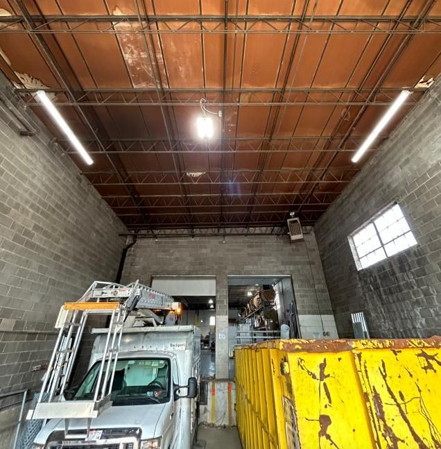 Interior of a loading dock with a truck, dumpster, and a metal beam ceiling.