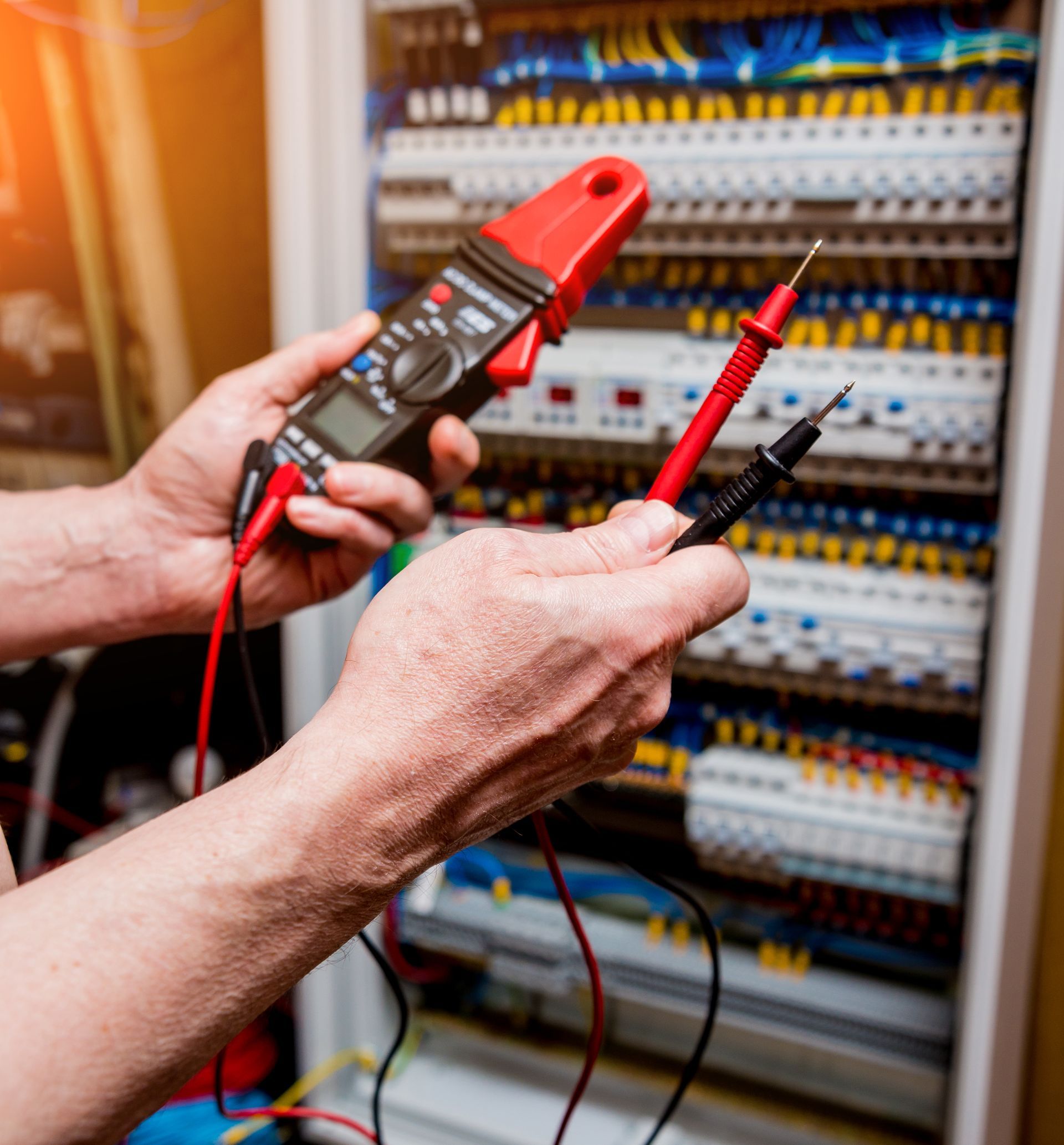 Electrician using a multimeter to test wiring in a control panel.