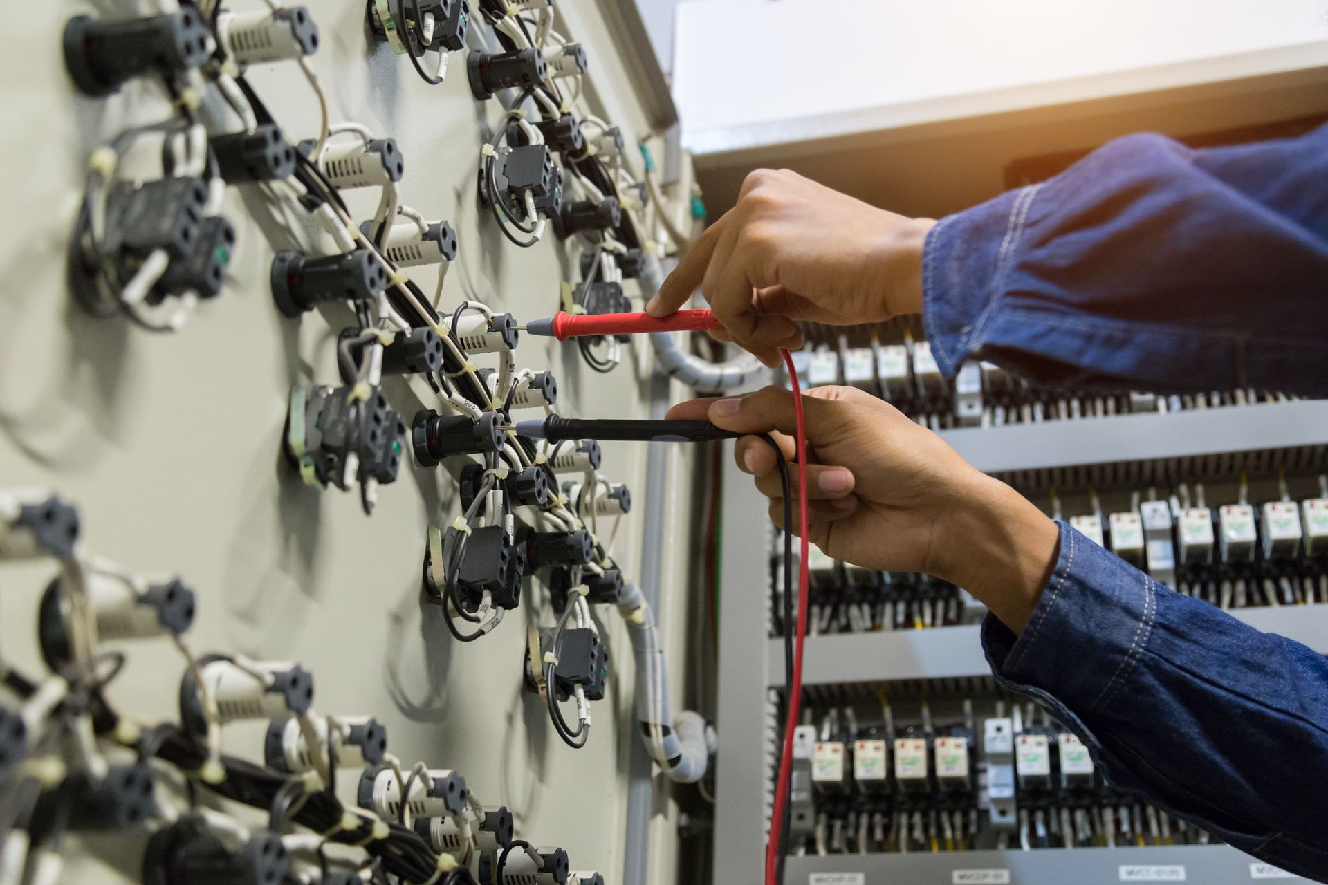 Hands of a person using a multimeter to test electrical wiring inside a control panel.