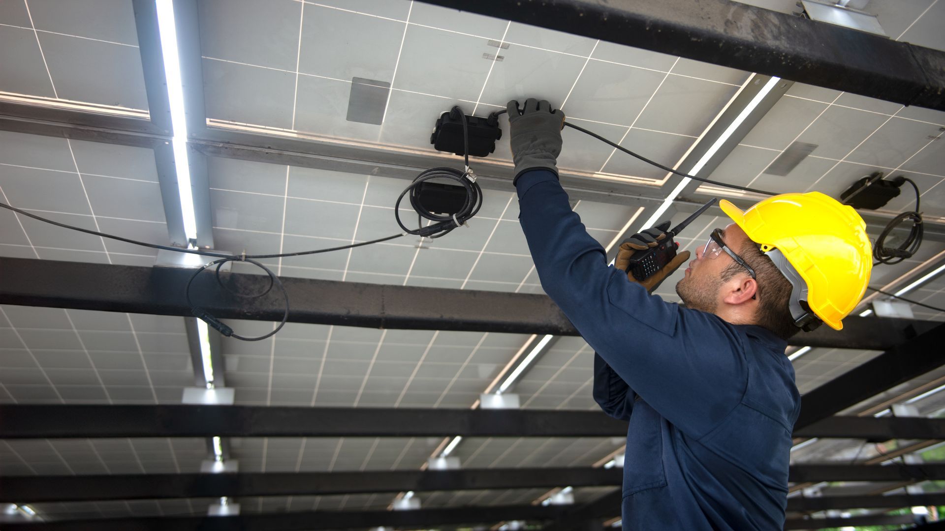 Solar panel installer in yellow helmet connecting wires.