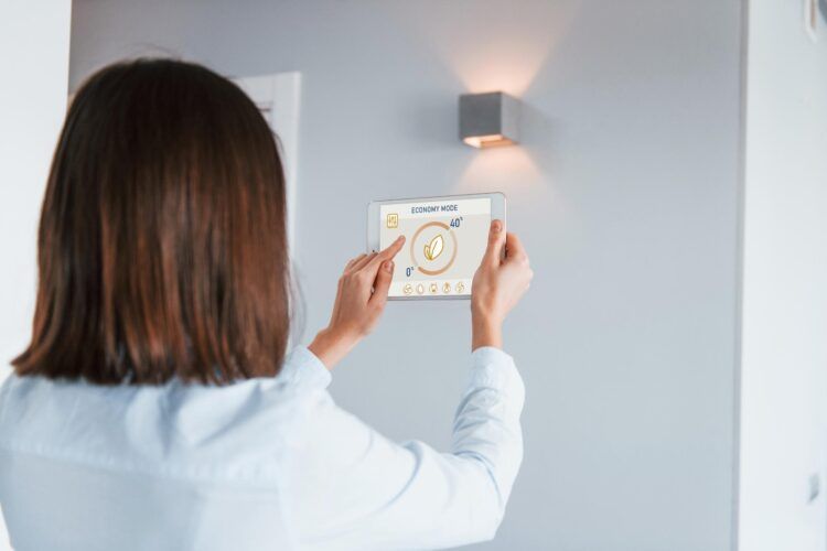 Woman using tablet to control a wall-mounted light. Indoors, gray wall, white doorframe.