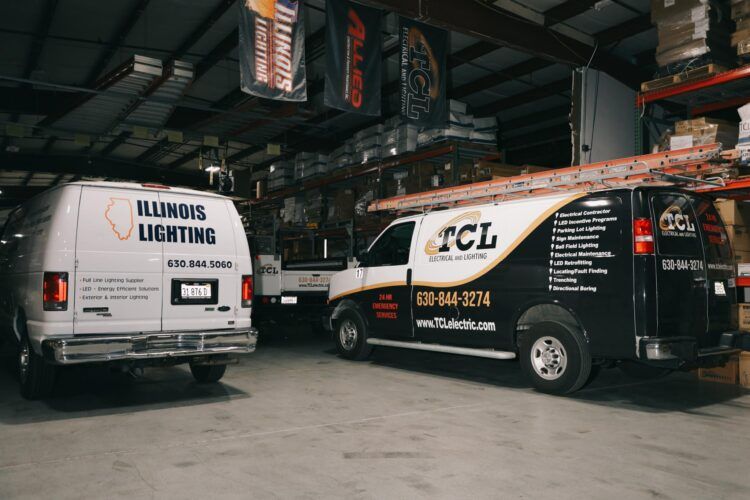 Two commercial vans, one white and one black, inside a warehouse. Vans are labeled with company logos and phone numbers.
