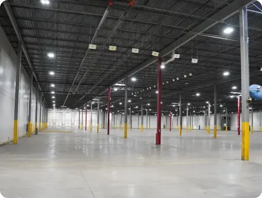 Empty warehouse interior with tall columns, fluorescent lights, and a concrete floor.