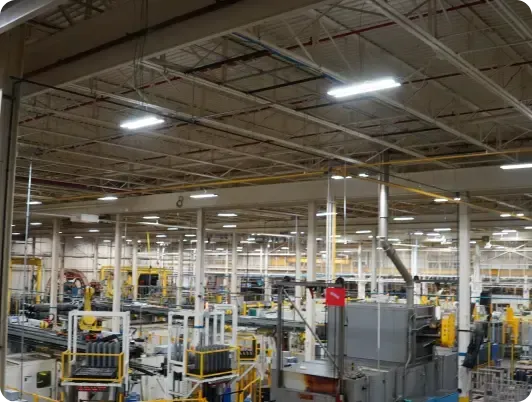 Factory interior with overhead lighting and equipment, workers in action.