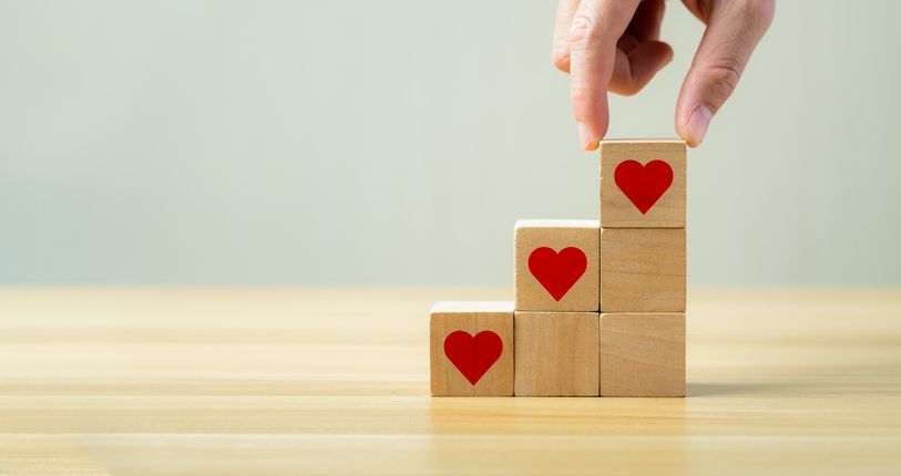 A person is stacking wooden blocks with hearts on them on a wooden table.