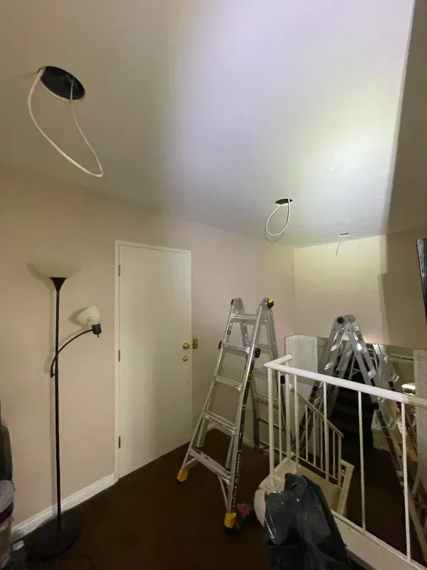 Room with two hanging ceiling light wires, a ladder, a door, and a floor lamp.