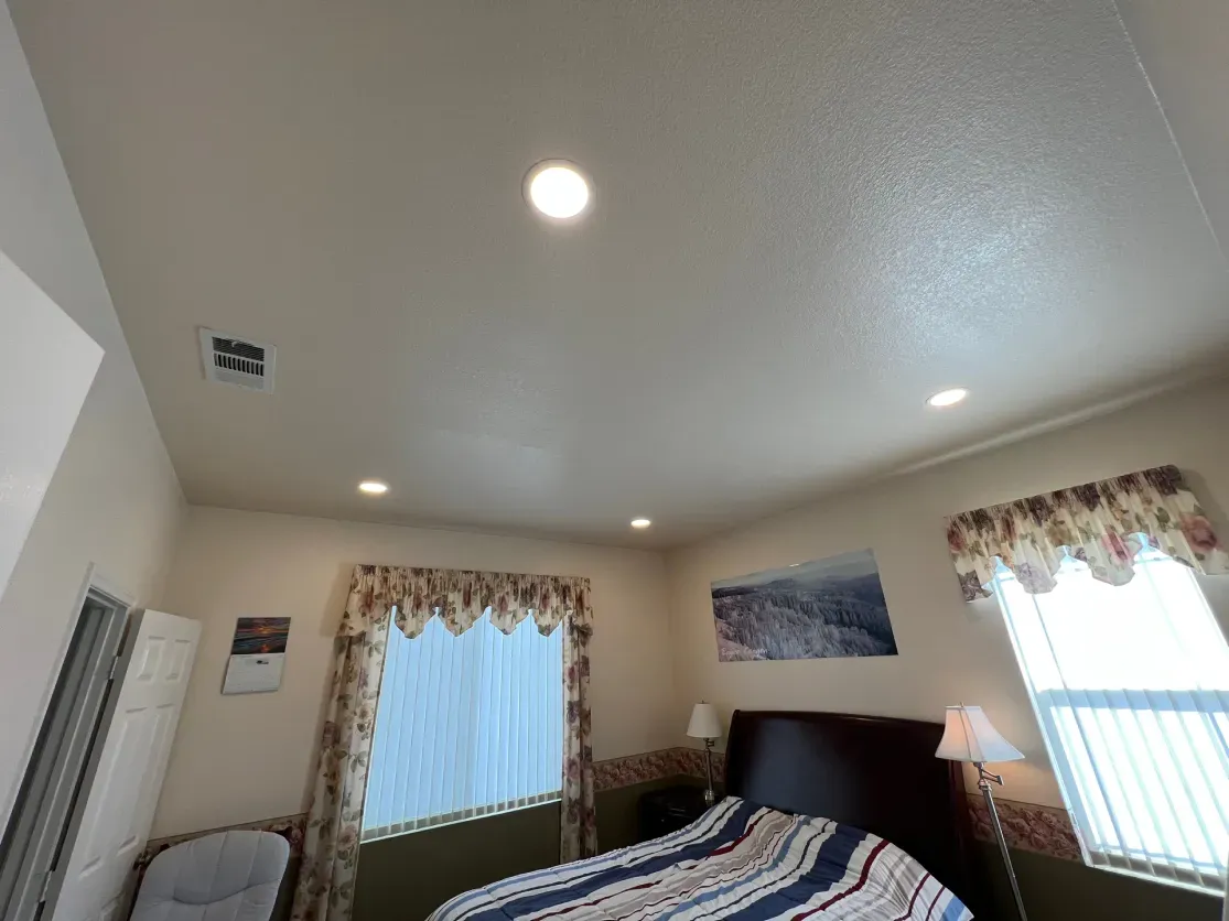 Bedroom interior with bed, windows, and recessed lighting.