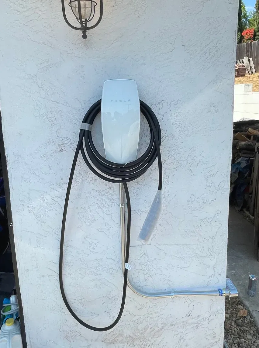 White EV charger mounted on stucco wall with a coiled black cable and gray connector.