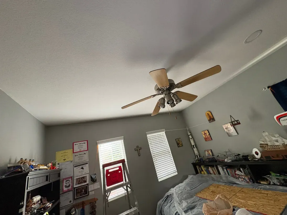 Ceiling fan in a gray bedroom, windows and shelves on the wall.