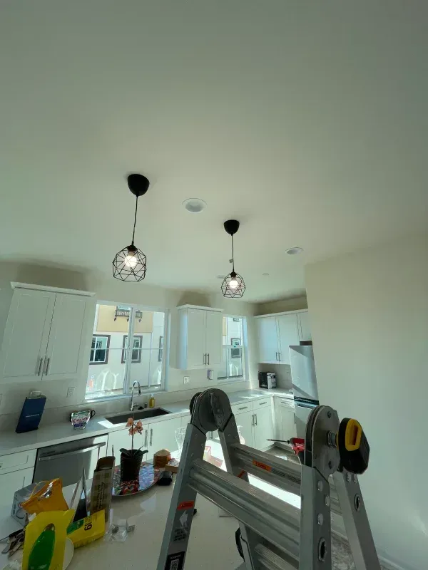 Kitchen with white cabinets, countertops, and two black pendant lights. A ladder is in the foreground.