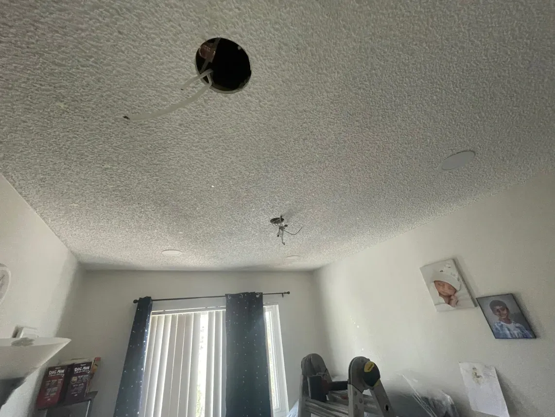 Ceiling with a large hole. Wires hang down. Room has white walls, curtains, and artwork.