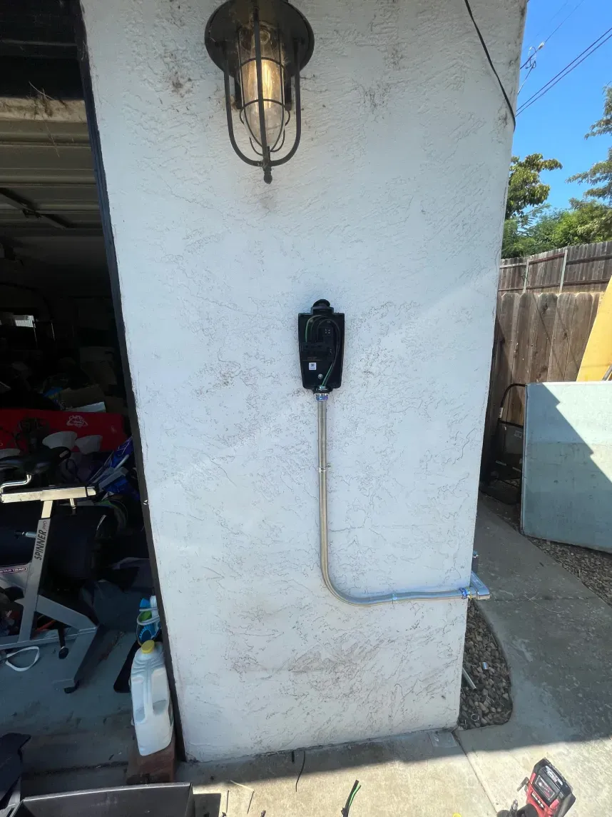 Electric vehicle charger mounted on a textured white wall beneath an outdoor light fixture.