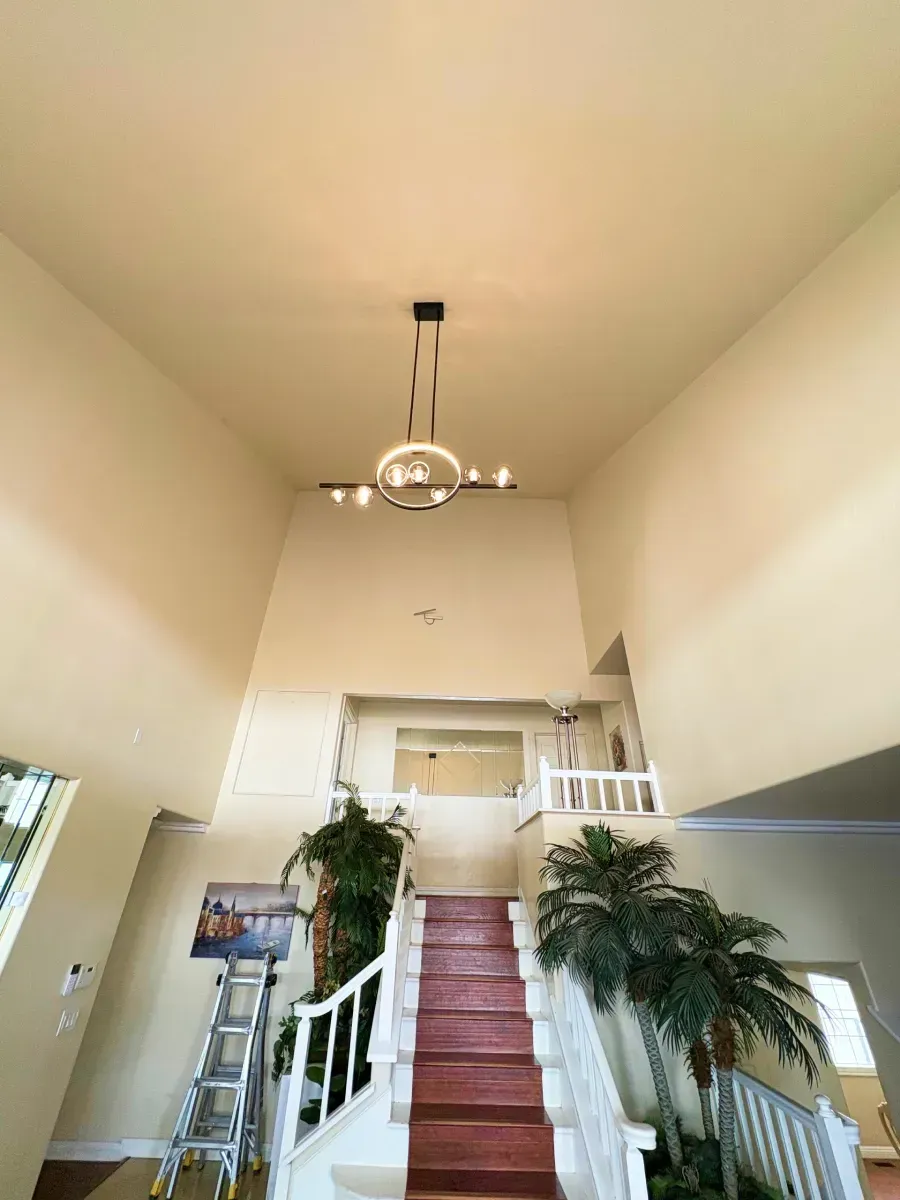 High-ceiling foyer with chandelier above staircase, red carpet, and greenery, bathed in soft light.