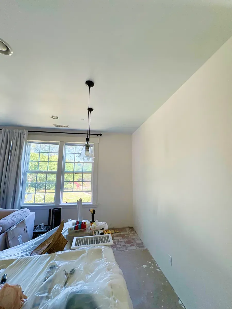 Room interior with freshly painted white walls, a window, and a hanging light fixture.