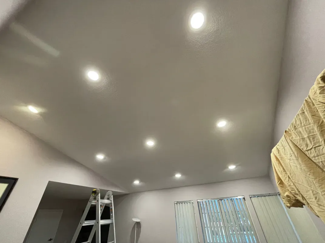 Angled ceiling with recessed lights, ladder, and partially visible window blinds.