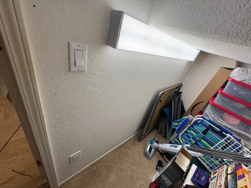 Wall with light switch and fluorescent light fixture, cluttered storage area.