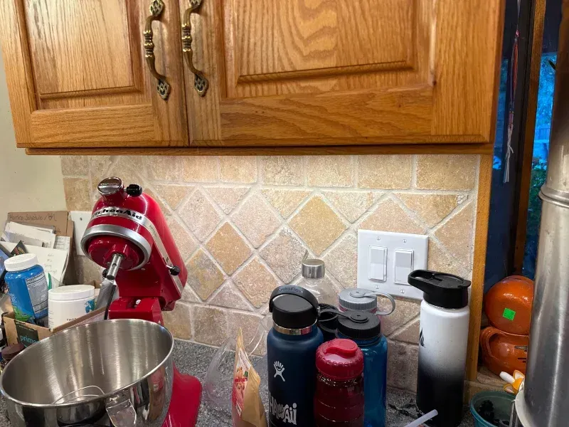 Red stand mixer on a kitchen counter with water bottles, under cabinets.