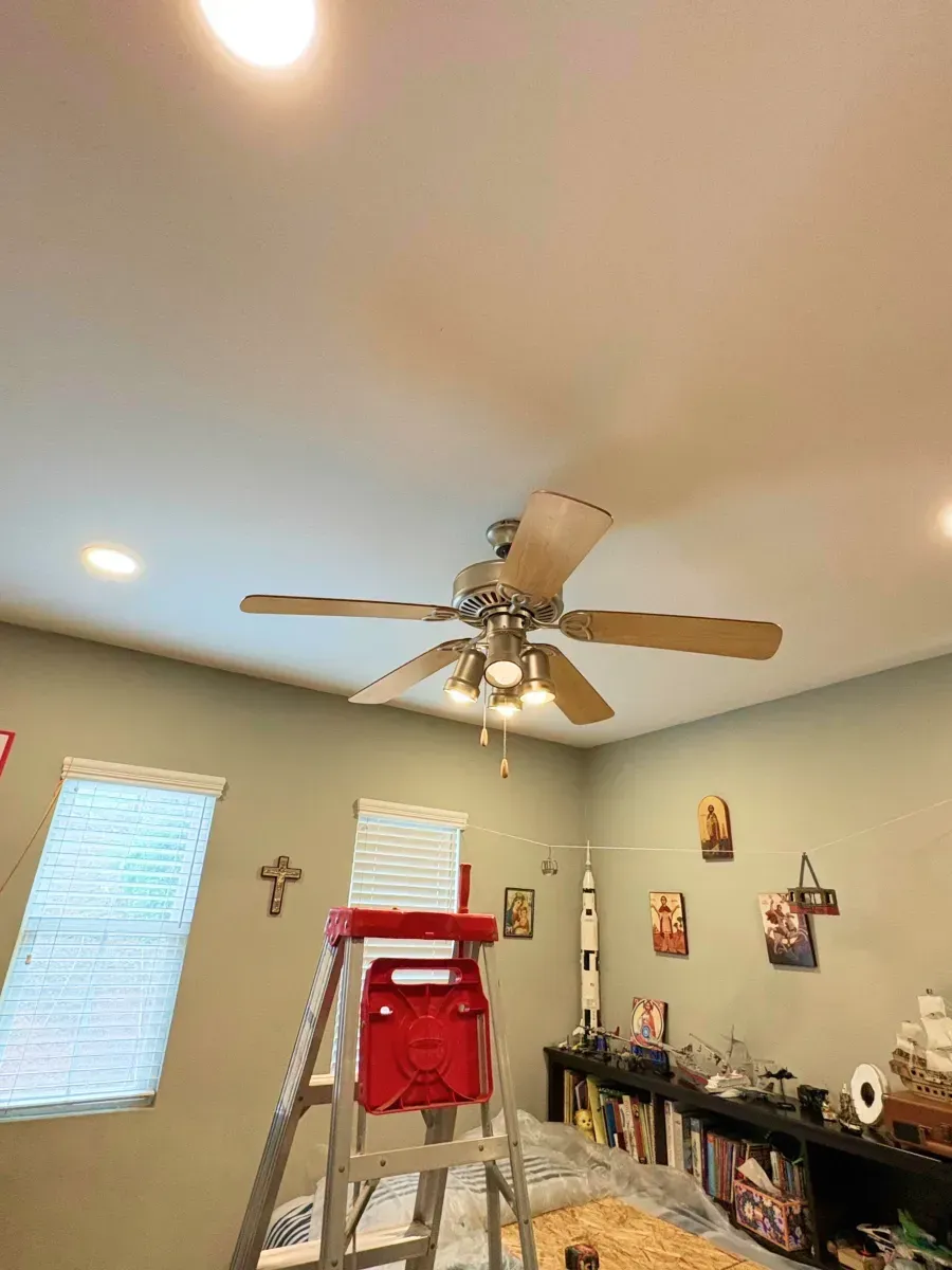 Ceiling fan in a room with a ladder; recessed lighting and wall decorations are visible.