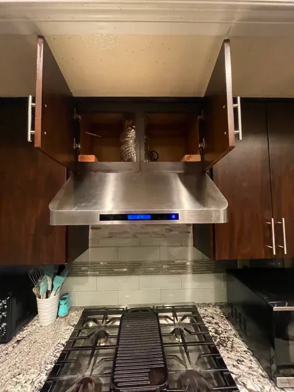 Range hood centered above a stove, with upper cabinets open, in a kitchen. Stainless steel.