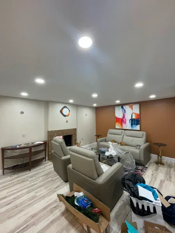 Living room with furniture, including a sofa, chairs, and a coffee table, with art on the walls and several recessed lights.
