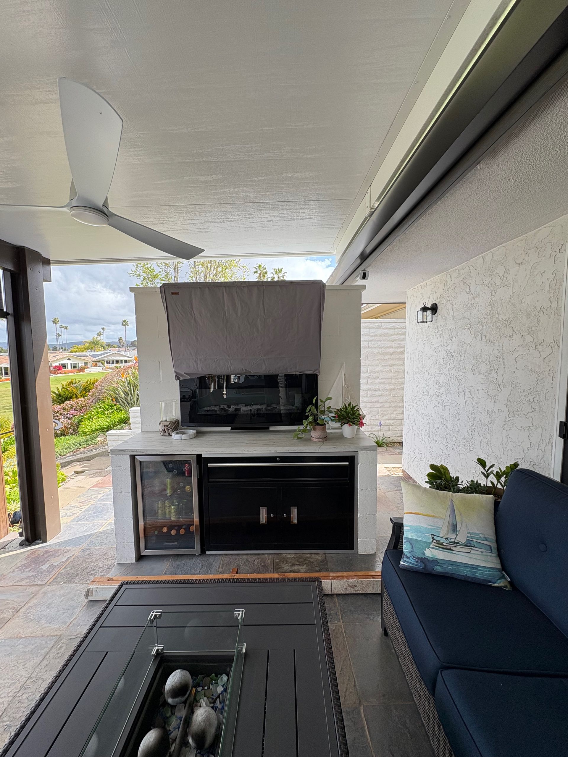 Outdoor patio with fireplace, built-in mini fridge, and seating. Gray concrete with blue sofa and pillows.
