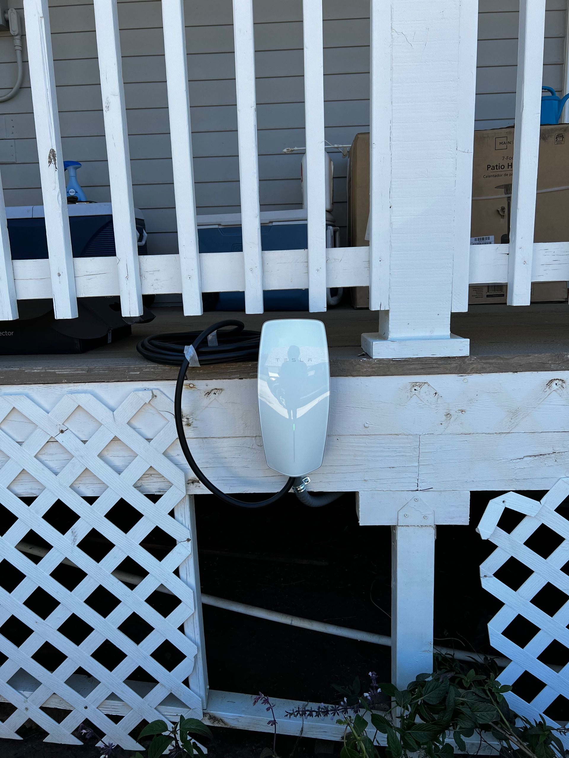 White electric vehicle charger mounted on a white porch post with black cable running to the ground.