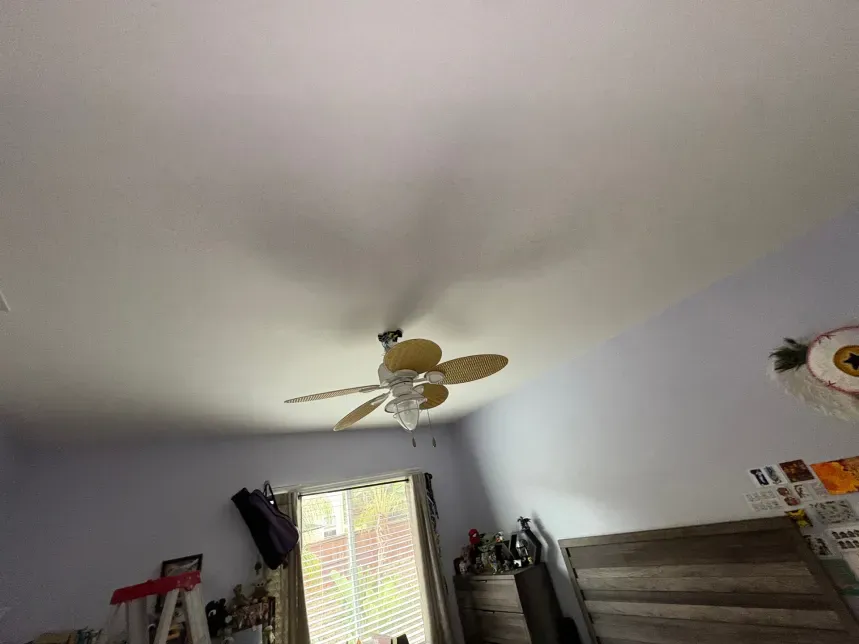 Ceiling fan in a bedroom with a window, bed, and decorative items.