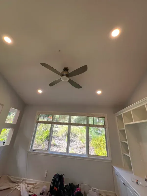 Ceiling with a fan, recessed lights, and a window overlooking greenery. Built-in shelving unit on the right.