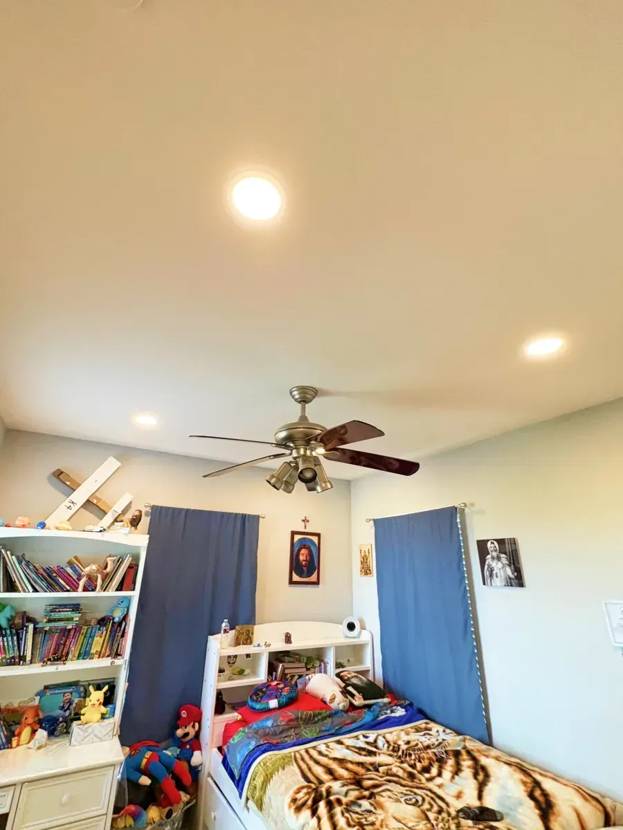 Bedroom with bed, bookshelf, ceiling fan, and blue curtains.