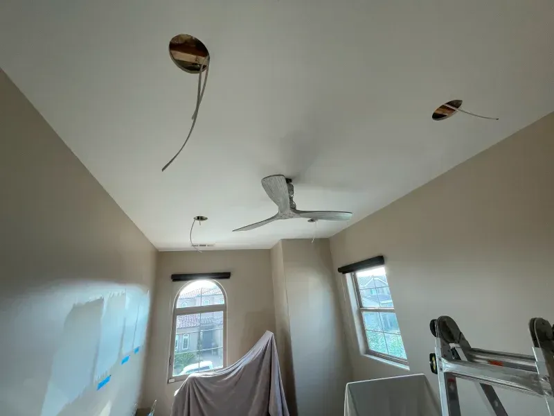 Ceiling with exposed wiring, a fan, two windows, and unfinished walls.