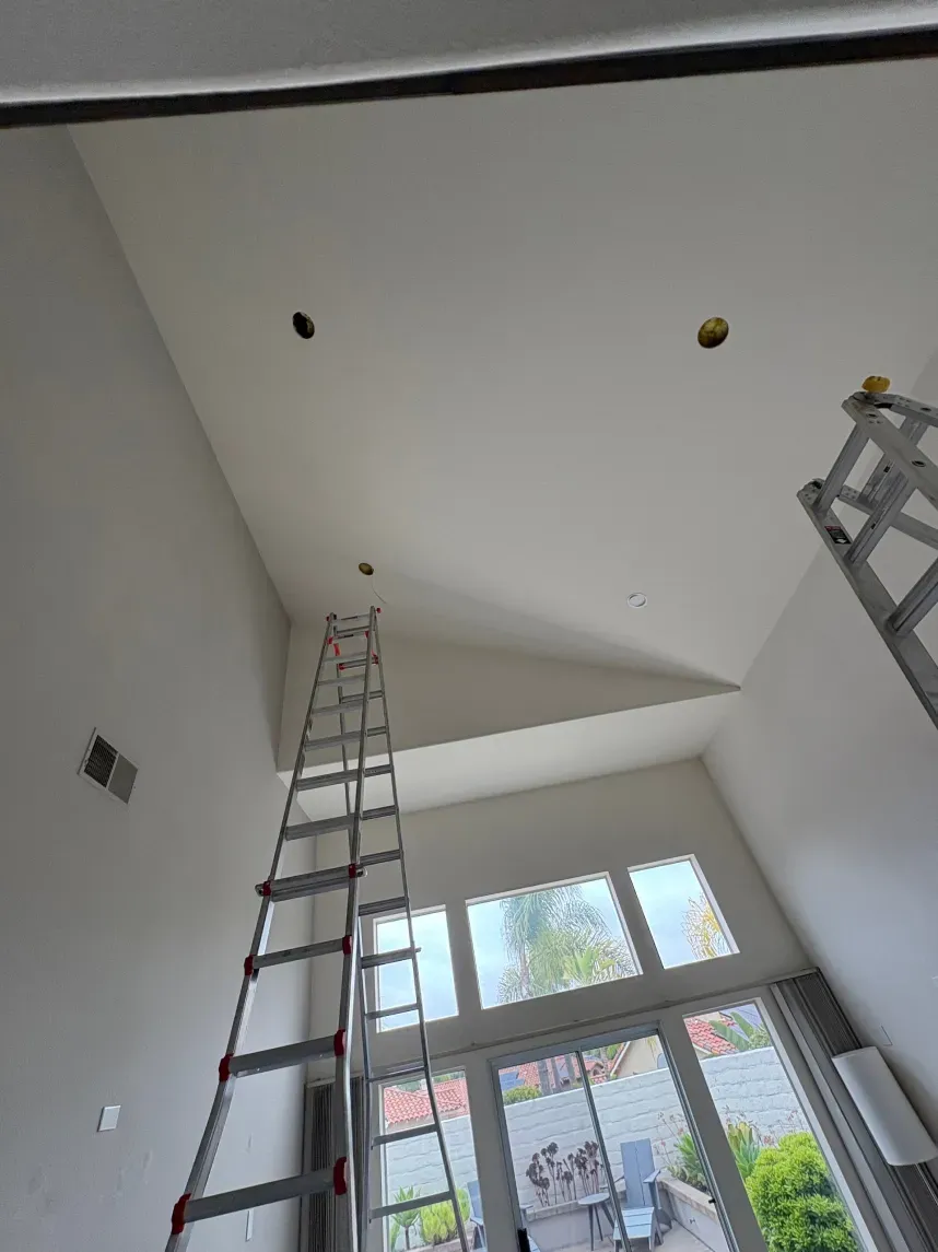 Interior view: Ladder against a high white ceiling with three holes, near windows.