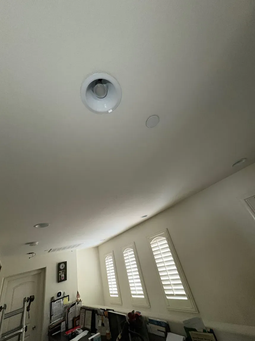 Angled ceiling with a recessed light fixture and windows with blinds.