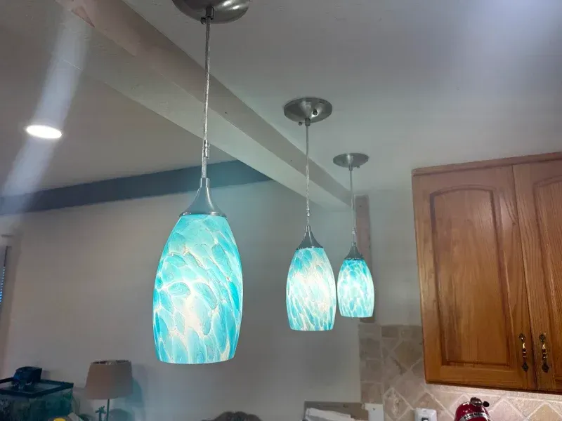 Three turquoise pendant lights hanging in a kitchen with wooden cabinets.