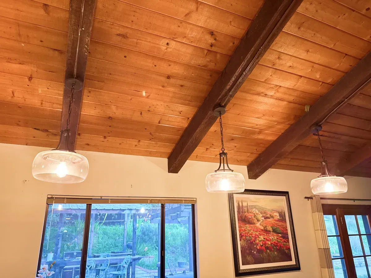Wooden ceiling with exposed beams and hanging pendant lights over a window and painting.
